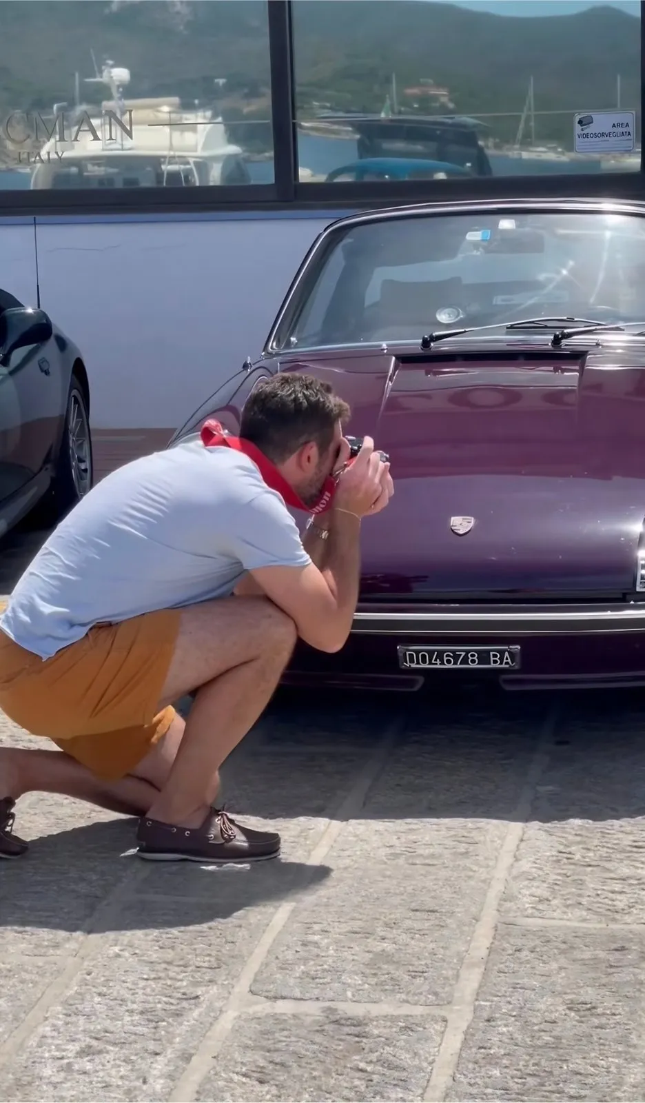 Giacomo, accovacciato, fotografa un’auto d’epoca vicino al porto