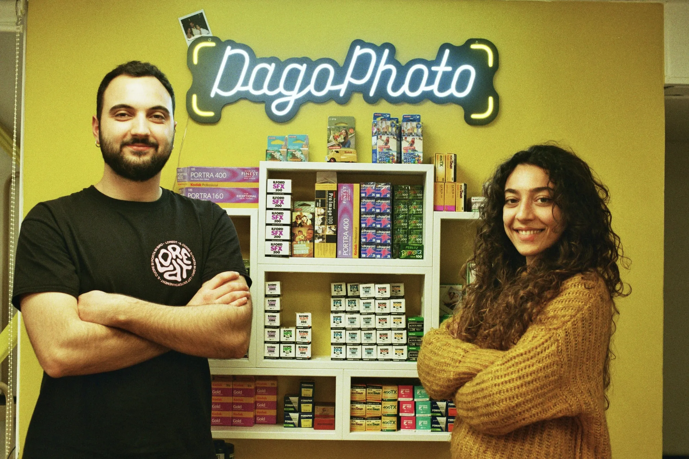 Agnese e Alessandro nel negozio, davanti all'insegna al neon e alle pellicole